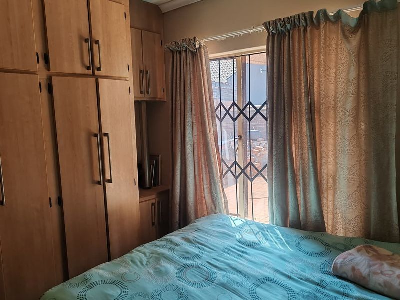 A bedroom featuring built-in wooden cupboards and a sliding door with a security gate, providing access to the exterior.