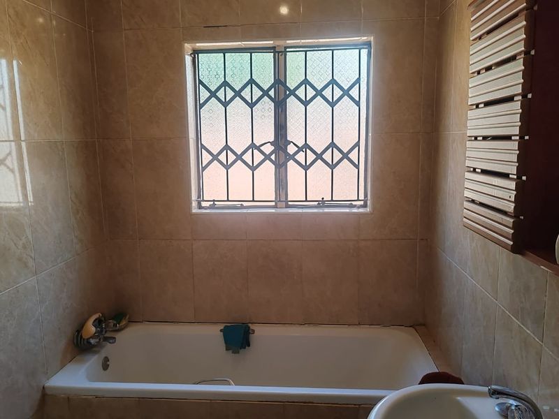 A functional bathroom featuring a built-in bathtub, ceramic wall tiling, and a window fitted with a security gate.