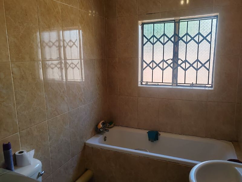A functional bathroom featuring a built-in bathtub, ceramic wall tiling, and a window fitted with security bars.