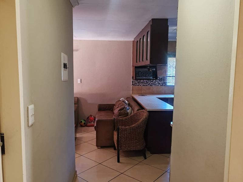 An open-plan living and kitchen area featuring tiled flooring and built-in cabinetry, viewed from an adjacent hallway.