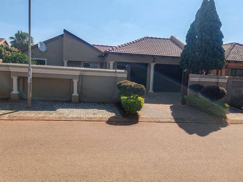 Front view of a residential property featuring a tiled roof, double garage, and a paved driveway enclosed by a perimeter wall with security spikes.