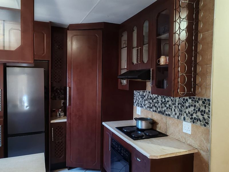 A functional kitchen featuring dark wood cabinetry, stone tile backsplash, built-in oven, and electric hob with an integrated extractor fan.