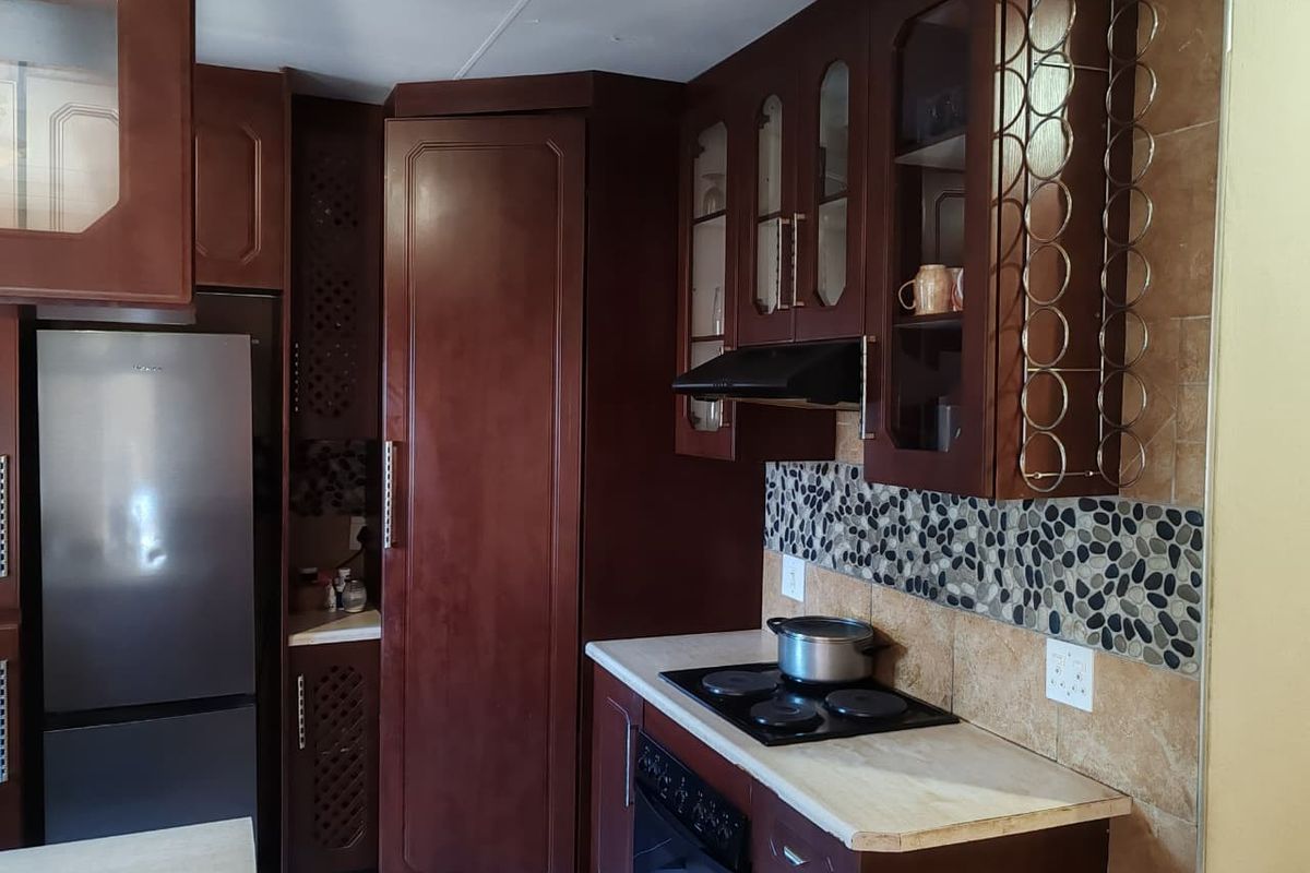 A functional kitchen featuring dark wood cabinetry, stone tile backsplash, built-in oven, and electric hob with an integrated extractor fan.
