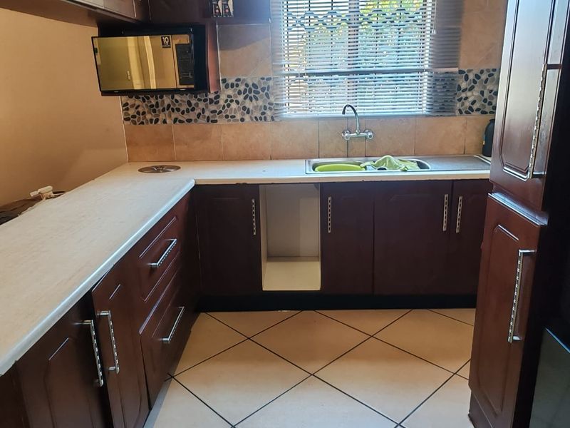 A functional kitchen featuring dark wood cabinetry, laminate countertops, a stainless steel sink, and tiled flooring with a dedicated space for an under-counter appliance.