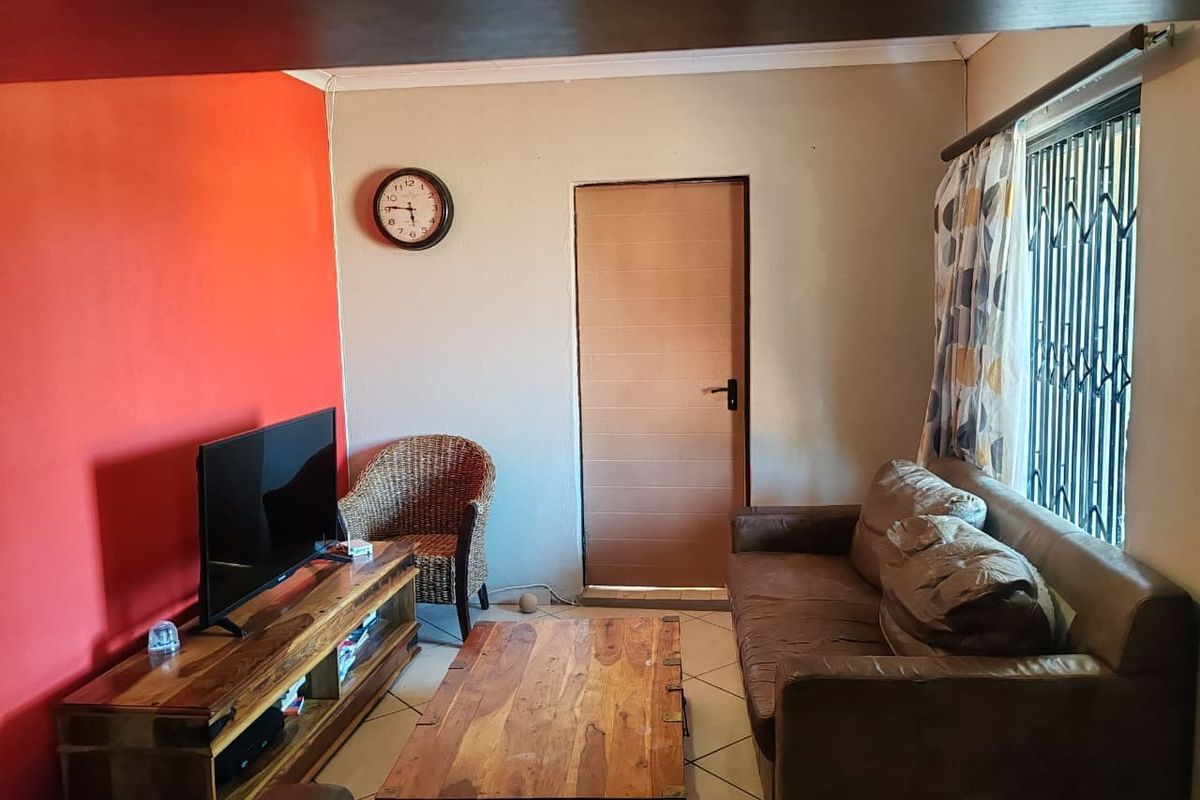 A living room featuring tiled flooring, a security gate on the window, and a bold accent wall.