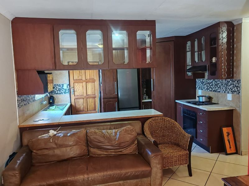 Open-plan kitchen and living area featuring dark wood cabinetry, tiled backsplash, and integrated appliances, offering a functional layout with potential for modern updates.