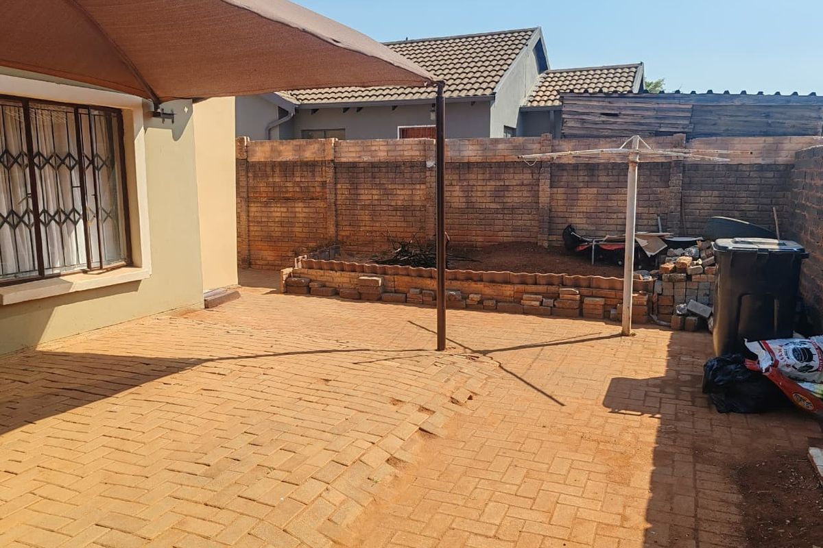 Rear exterior area featuring a paved patio, brick boundary wall, and a shade sail structure, offering potential for outdoor living space improvement.