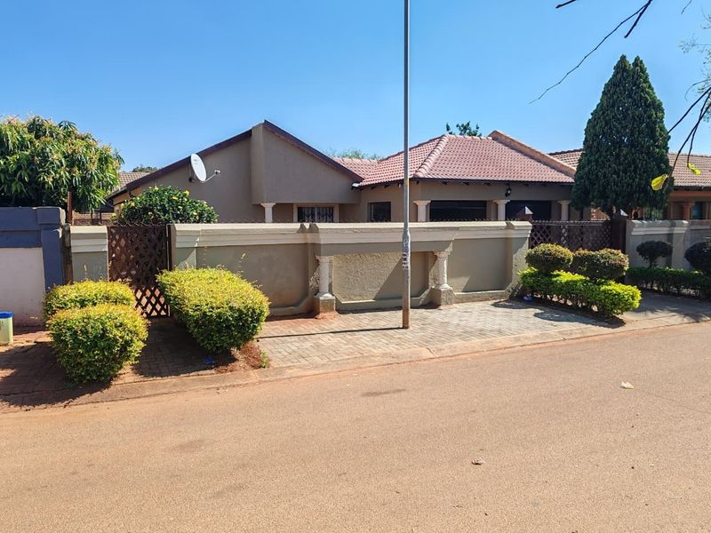 Front view of a residential house featuring a tiled roof, perimeter wall, and paved driveway area.