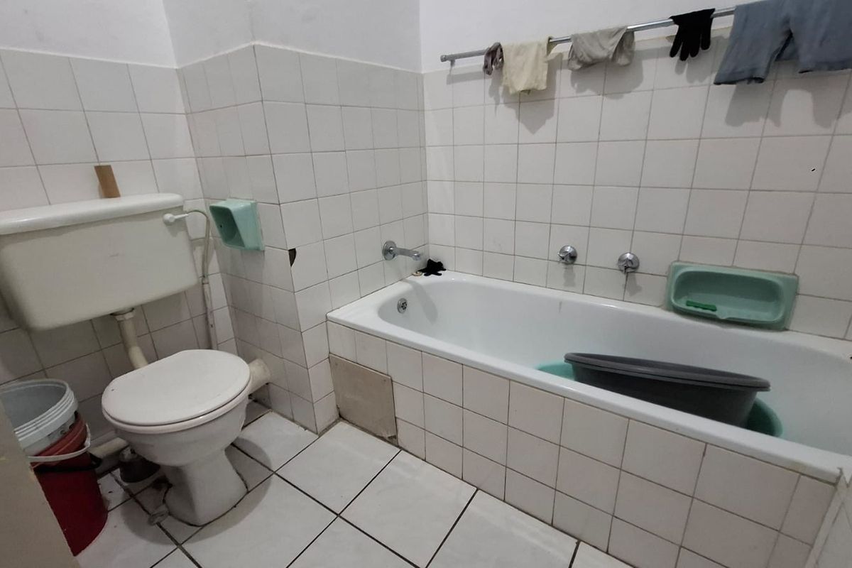 A dated bathroom featuring a standard bathtub, toilet, and white ceramic wall and floor tiling, requiring cosmetic updates to improve its overall condition.