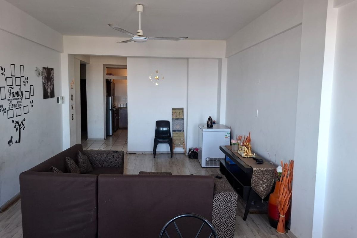 A spacious living area featuring laminate flooring and a ceiling fan, with an open-plan layout leading towards the kitchen area.