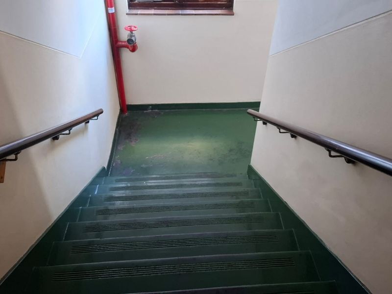 A functional apartment building stairwell featuring painted concrete steps, wall-mounted handrails, and an exposed fire hydrant pipe.