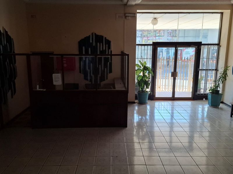 A functional apartment building entrance lobby featuring tiled flooring, a reception counter, and glass double doors leading to the street.