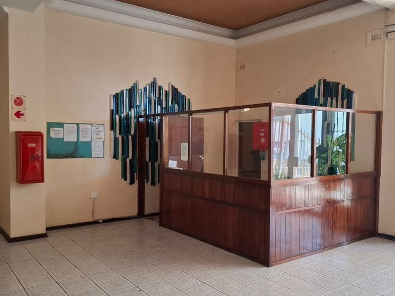 A spacious apartment building entrance lobby featuring a built-in reception desk, tiled flooring, and integrated fire safety equipment.