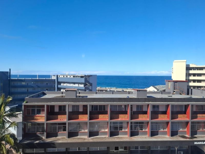 An elevated view overlooking surrounding apartment buildings with a clear horizon line of the ocean in the distance.