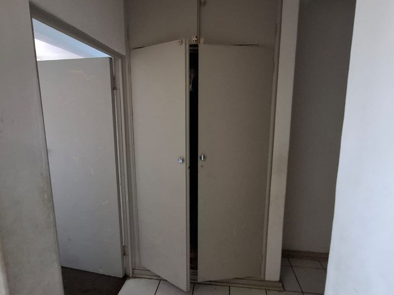 A functional hallway area featuring tiled flooring and a built-in cupboard with double doors, showing signs of wear and tear.