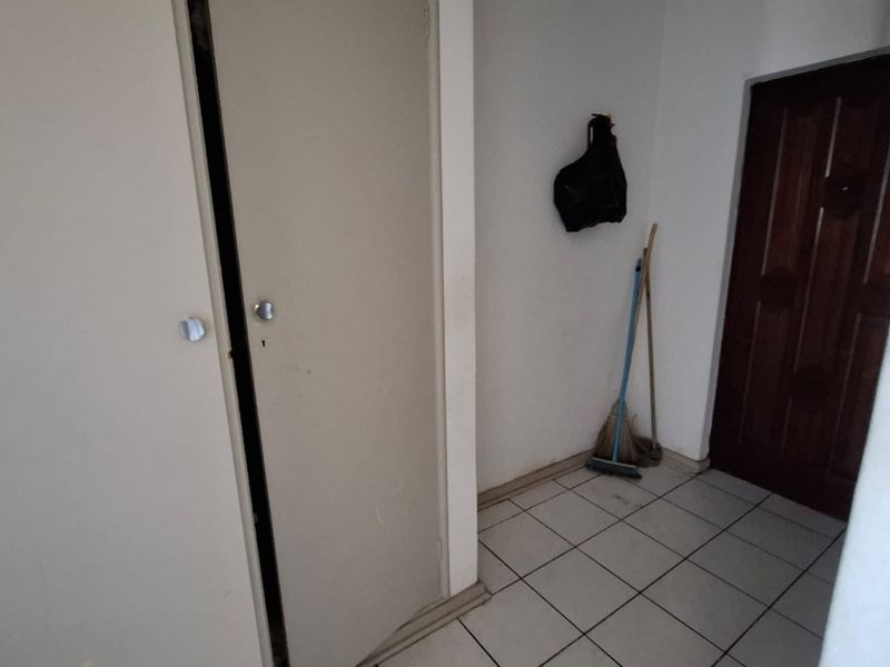 A functional hallway area featuring tiled flooring, a built-in cupboard, and a solid timber door, providing access to other parts of the apartment.