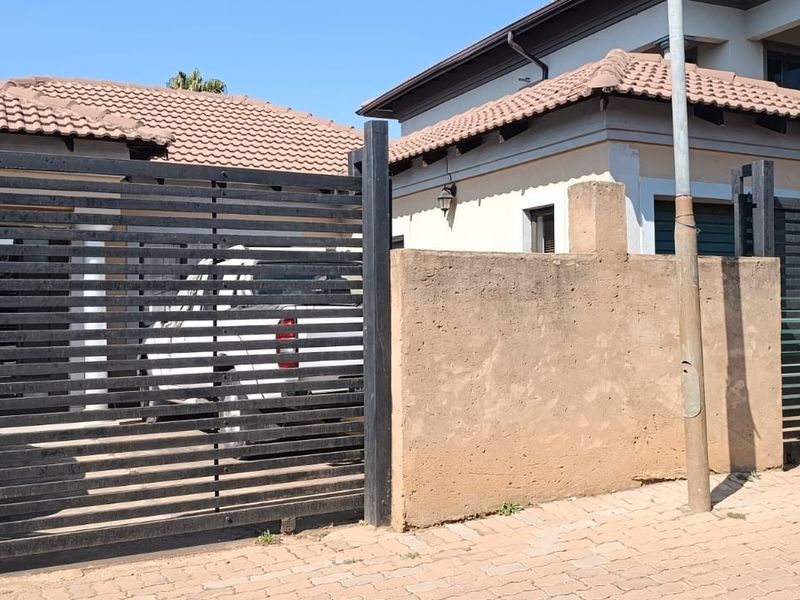 Front view of the property featuring a slatted metal gate, concrete boundary wall, and tiled roof structure.