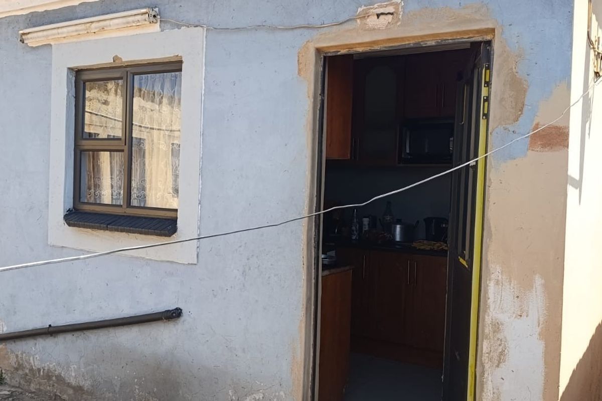 Rear exterior view of the property showing unfinished plasterwork, peeling paint, and access to the kitchen area.