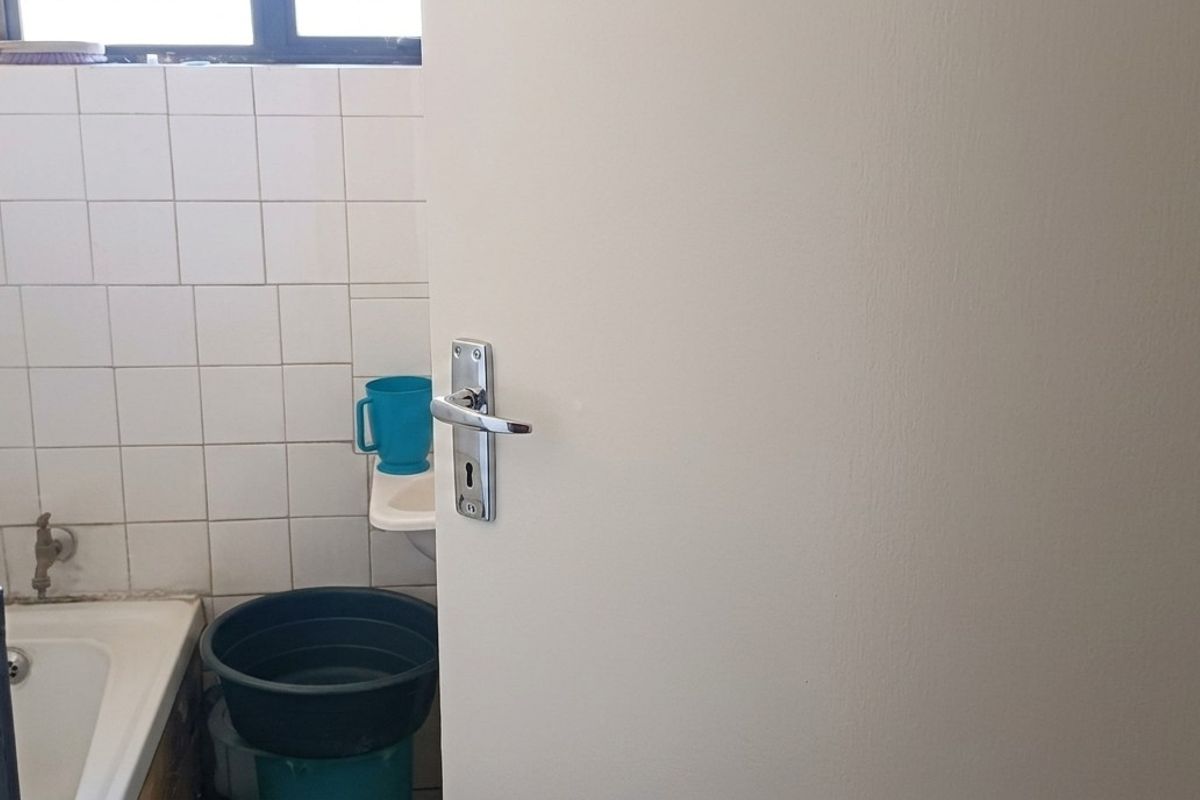 A compact bathroom featuring a bathtub, wall tiling, and a small basin, currently in need of cosmetic updates.