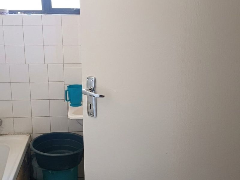 A compact bathroom featuring a bathtub, wall tiling, and a small basin, currently in need of cosmetic updates.