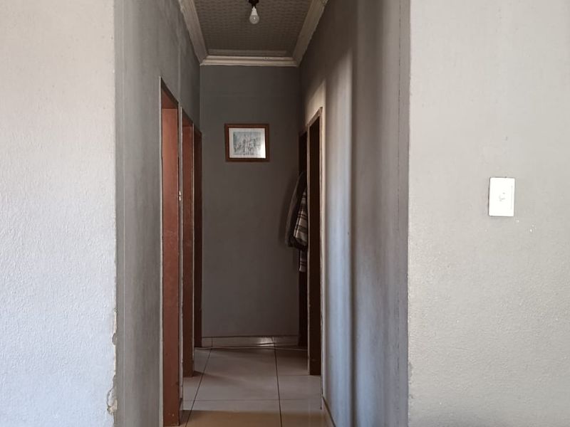 A narrow interior hallway featuring tiled flooring and textured ceiling, connecting multiple rooms within the property.