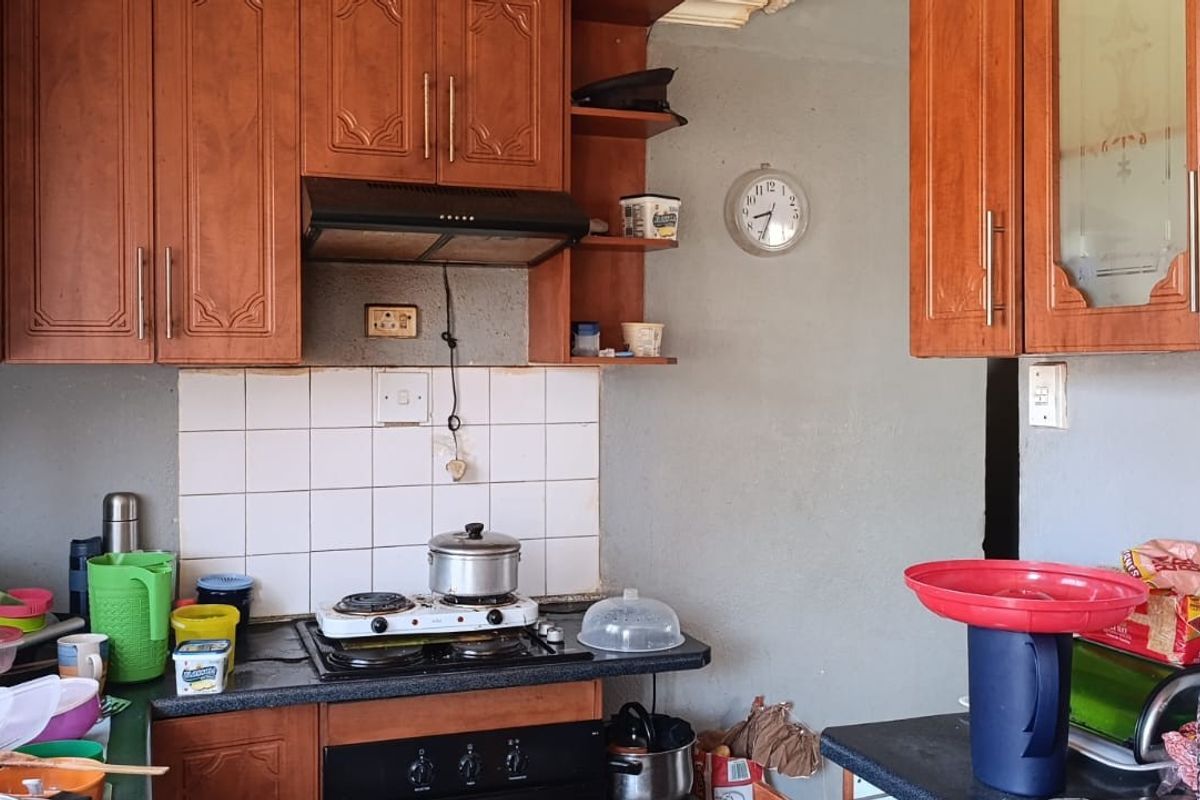 A dated kitchen featuring wooden cabinetry, a built-in oven, hob, and extractor fan with a tiled splashback.