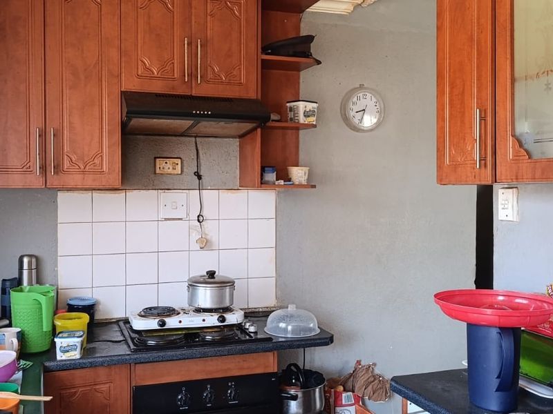 A dated kitchen featuring wooden cabinetry, a built-in oven, hob, and extractor fan with a tiled splashback.