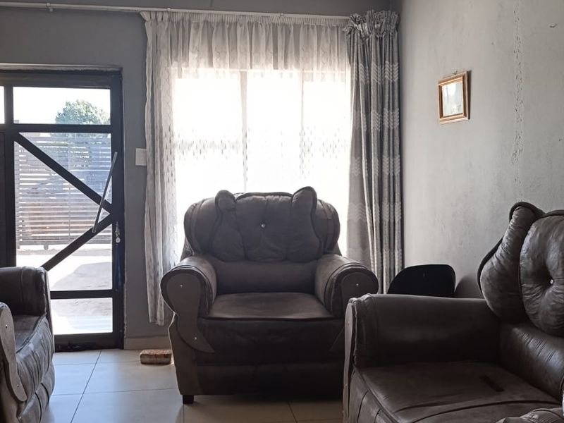 A living room featuring tiled flooring, a large window, and an aluminium framed glass door leading to the exterior.