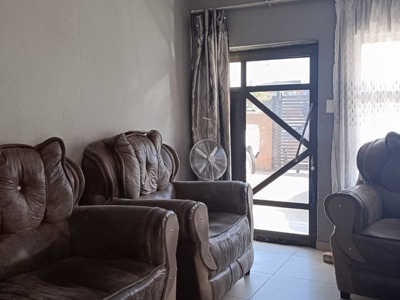 A living room area featuring tiled flooring, a glass panel door, and a large window, showing signs of wear on the wall surfaces.