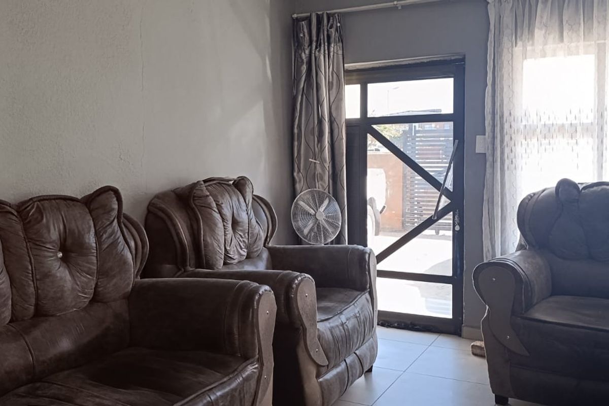 A living room area featuring tiled flooring, a glass panel door, and a large window, showing signs of wear on the wall surfaces.