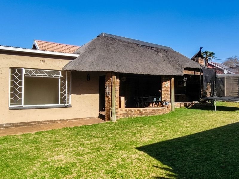 Rear garden view featuring a covered patio area with a thatched roof, brick pillars, and a well-maintained lawn with perimeter boundary walling.