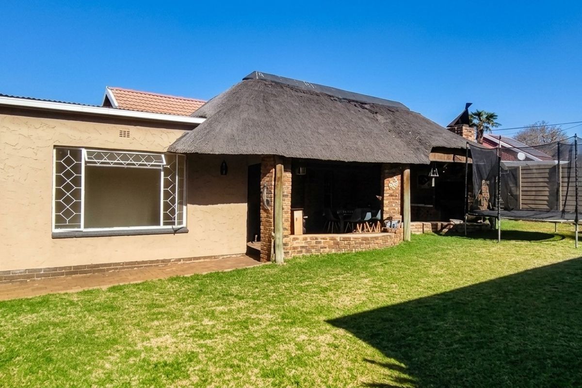 Rear garden view featuring a covered patio area with a thatched roof, brick pillars, and a well-maintained lawn with perimeter boundary walling.
