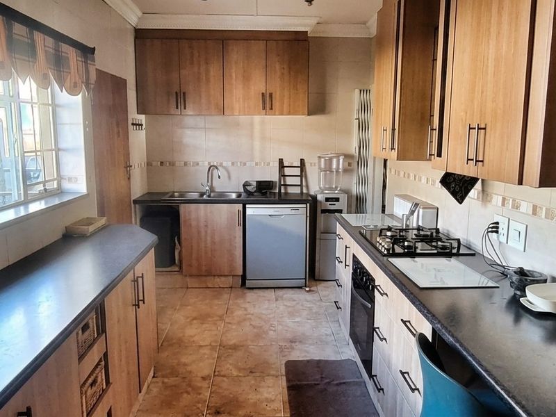 A functional kitchen featuring wood-finish cabinetry, dark laminate countertops, a gas hob, built-in oven, and tiled flooring with a neutral backsplash.