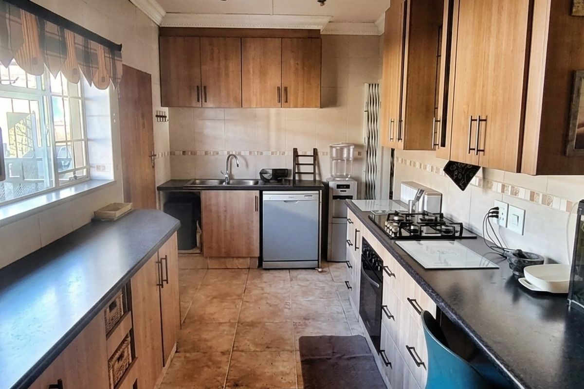 A functional kitchen featuring wood-finish cabinetry, dark laminate countertops, a gas hob, built-in oven, and tiled flooring with a neutral backsplash.