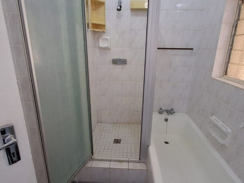 A dated bathroom featuring a separate shower cubicle and a bathtub with tiled finishes and a louvered window.