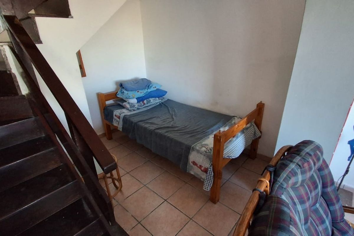 A bedroom space situated beneath a staircase, featuring tiled flooring and neutral wall finishes.