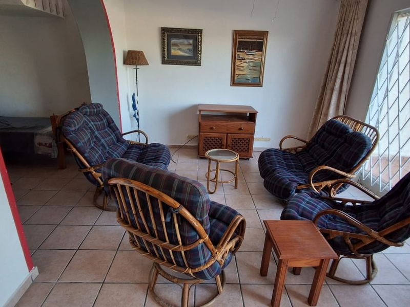 A living room area featuring tiled flooring, an arched entryway, and a security gate over the window, offering a functional and well-lit space.
