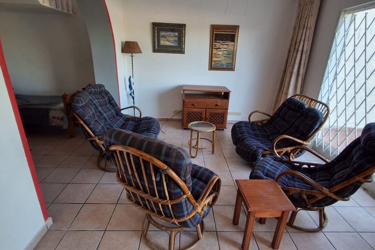 A living room area featuring tiled flooring, an arched entryway, and a security gate over the window, offering a functional and well-lit space.