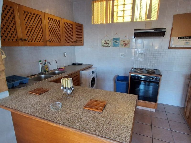 A functional kitchen featuring wooden cabinetry, a double bowl sink, a freestanding oven with extractor fan, and tiled finishes throughout.