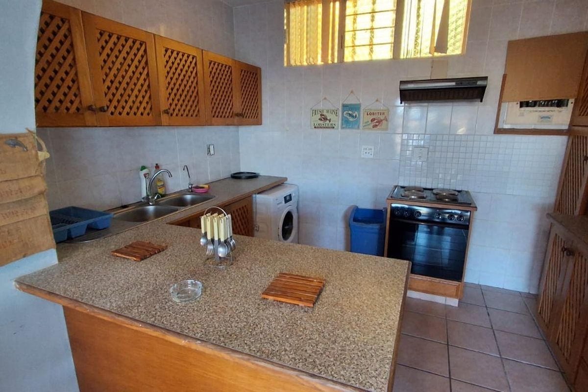 A functional kitchen featuring wooden cabinetry, a double bowl sink, a freestanding oven with extractor fan, and tiled finishes throughout.
