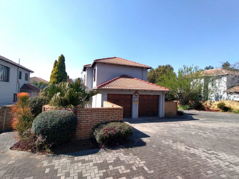 Front view of a townhouse featuring a double garage, paved driveway, and brick boundary wall in a well-maintained residential setting.