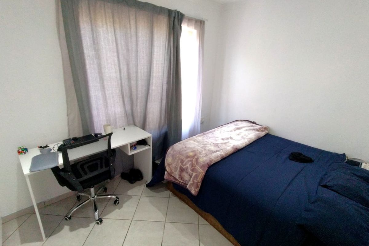 A functional bedroom featuring tiled flooring and large windows with curtain rails, providing a neutral space ready for personalization.
