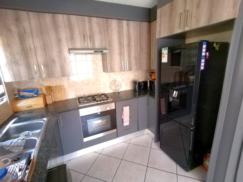 Modern kitchen featuring dark grey and wood-grain cabinetry, granite countertops, a gas hob, built-in oven, and tiled flooring.