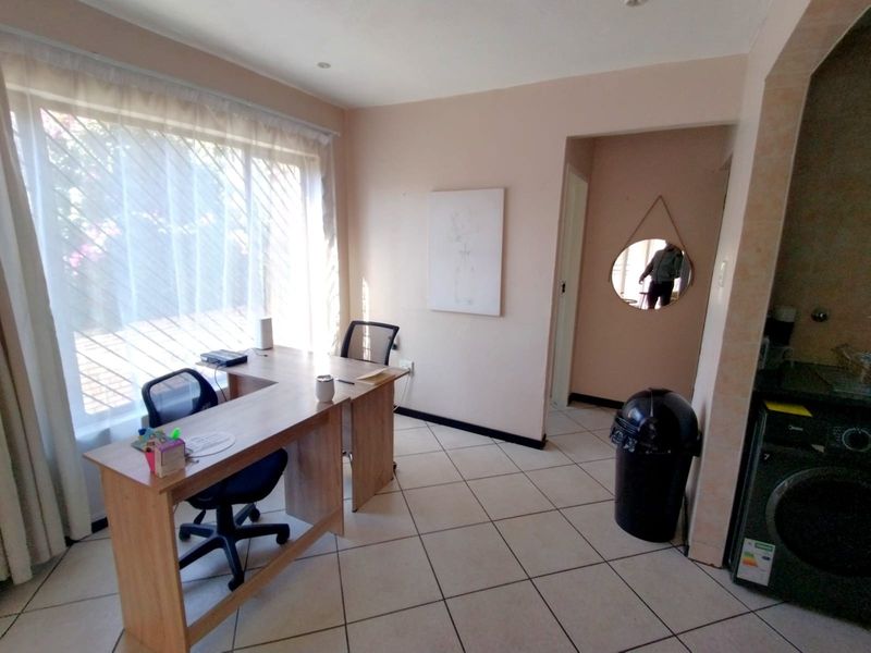 A functional office space featuring tiled flooring and recessed lighting, with an adjacent area suitable for laundry appliances.