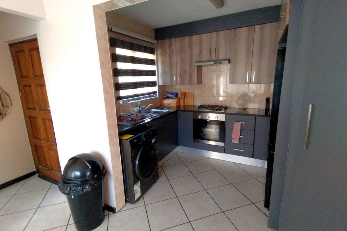 Compact kitchen featuring modern two-tone cabinetry, built-in gas hob, electric oven, extractor fan, and tiled flooring with integrated laundry appliance space.