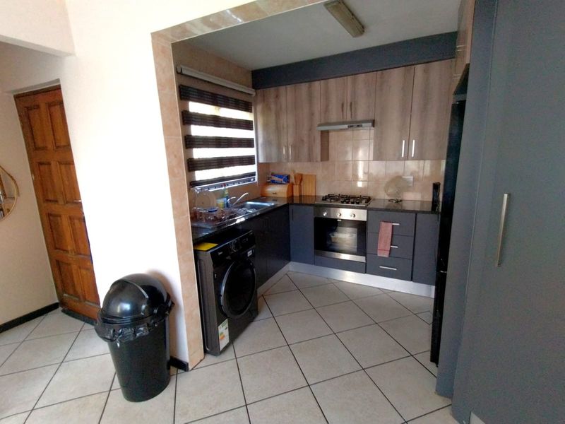 Compact kitchen featuring modern two-tone cabinetry, built-in gas hob, electric oven, extractor fan, and tiled flooring with integrated laundry appliance space.
