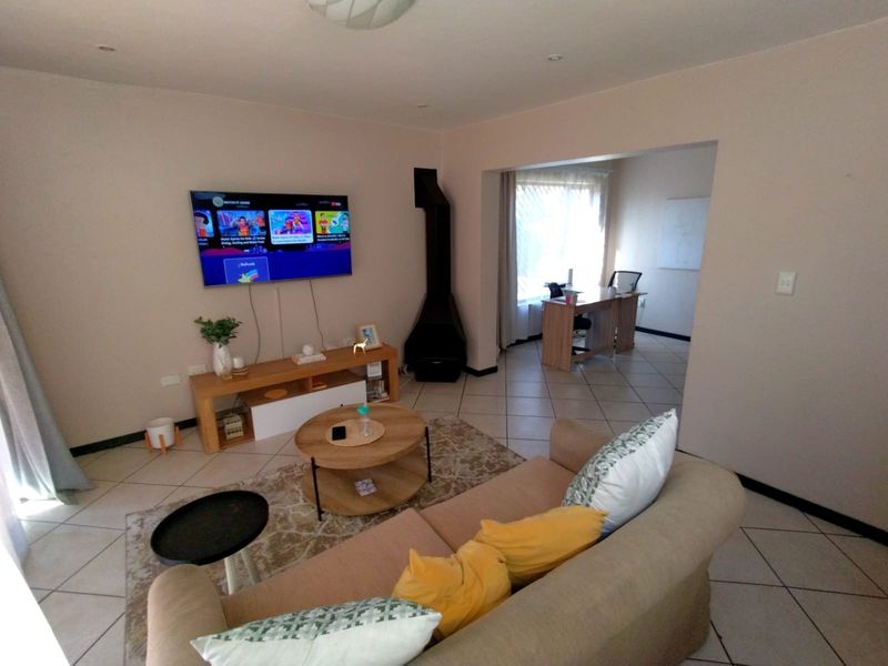 Open plan living area featuring ceramic floor tiles, a freestanding fireplace, and an adjoining space suitable for a home office or study.