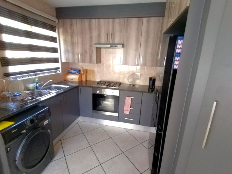 A functional kitchen featuring modern two-tone cabinetry, granite-look countertops, a gas hob, built-in oven, and tiled flooring with a convenient laundry connection.