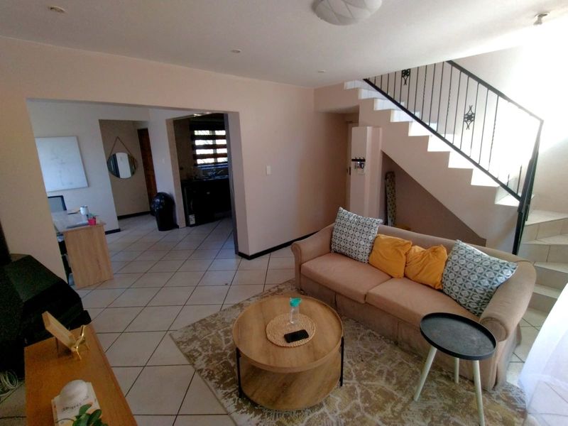 Open plan living area featuring tiled flooring, recessed lighting, and a staircase with a wrought iron balustrade, leading to a kitchen area.