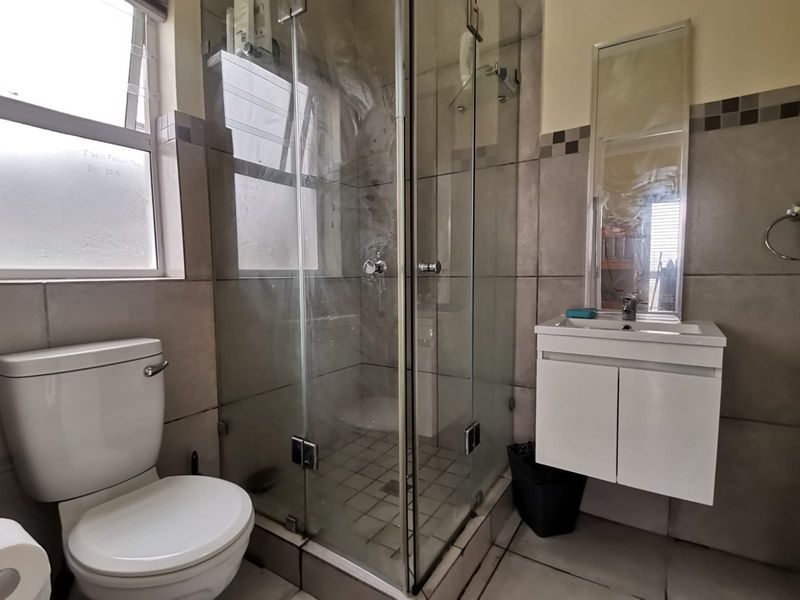 A functional bathroom featuring a glass-enclosed shower, wall-mounted vanity with integrated mirror, and neutral tiled finishes throughout.
